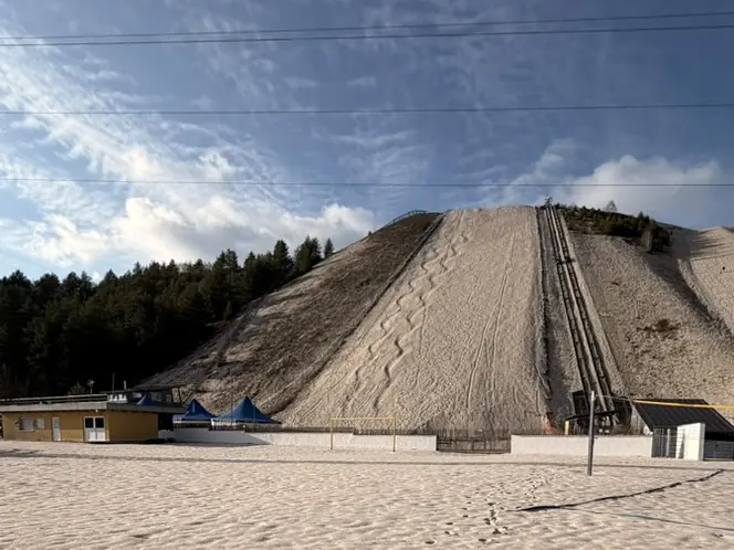 Fußspuren im Sand, dahinter der Monte Kaolino mit Sommerrodelbahn