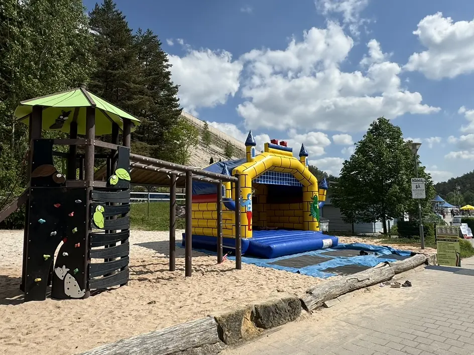 Spielplatz mit Klettergerüst und Hüpfburg im Sand neben dem Lokal