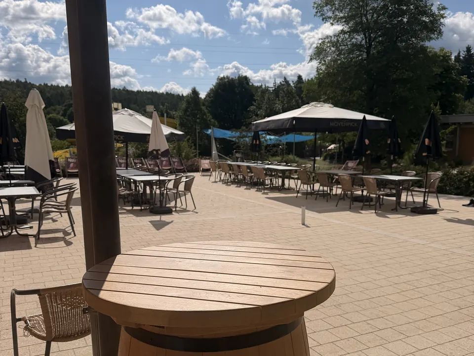 Stehtisch aus einem Holzfass auf der Terrasse, dahinter Sonnenschirme