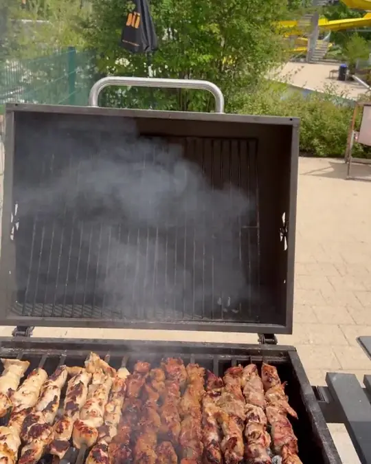 Grill mit Fleischspießen auf der Terrasse, Rauch steigt auf